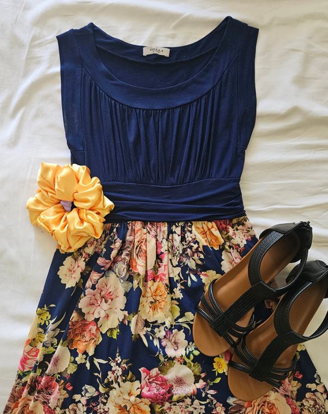 Navy floral dress styled with golden yellow satin scrunchies and black sandals on a white bedspread.