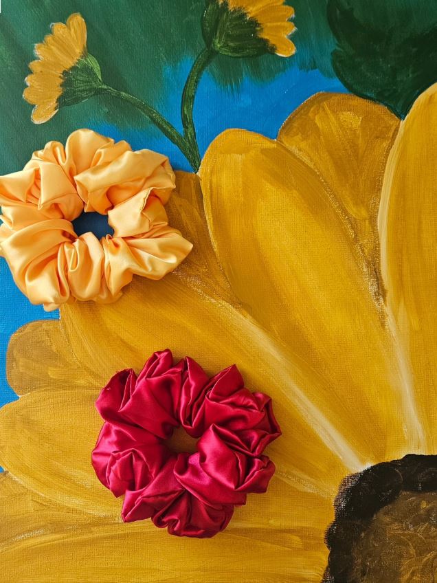 Golden yellow and deep red satin scrunchies arranged on a colorful sunflower painting.